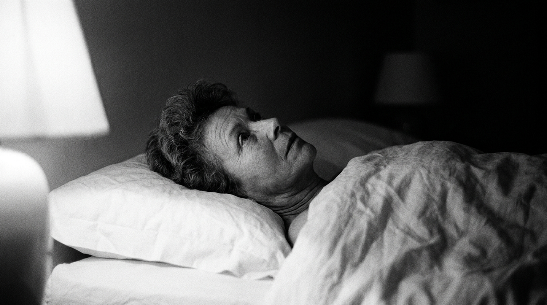 Femme d'une cinquantaine d'années allongée éveillée dans son lit la nuit, photographie en noir et blanc