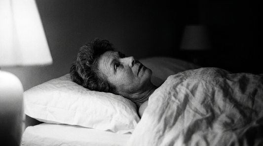 Femme d'une cinquantaine d'années allongée éveillée dans son lit la nuit, photographie en noir et blanc