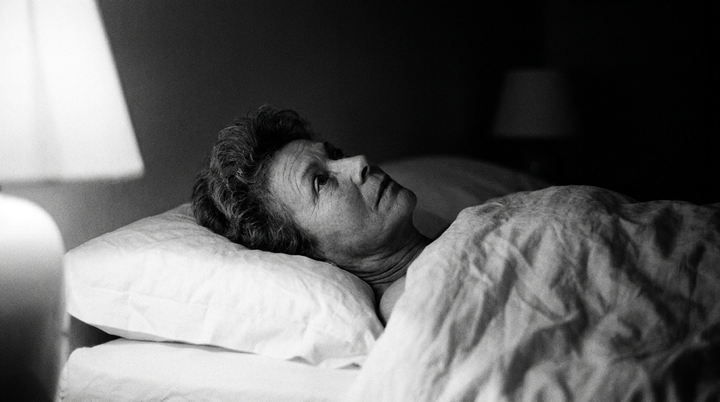 Femme d'une cinquantaine d'années allongée éveillée dans son lit la nuit, photographie en noir et blanc